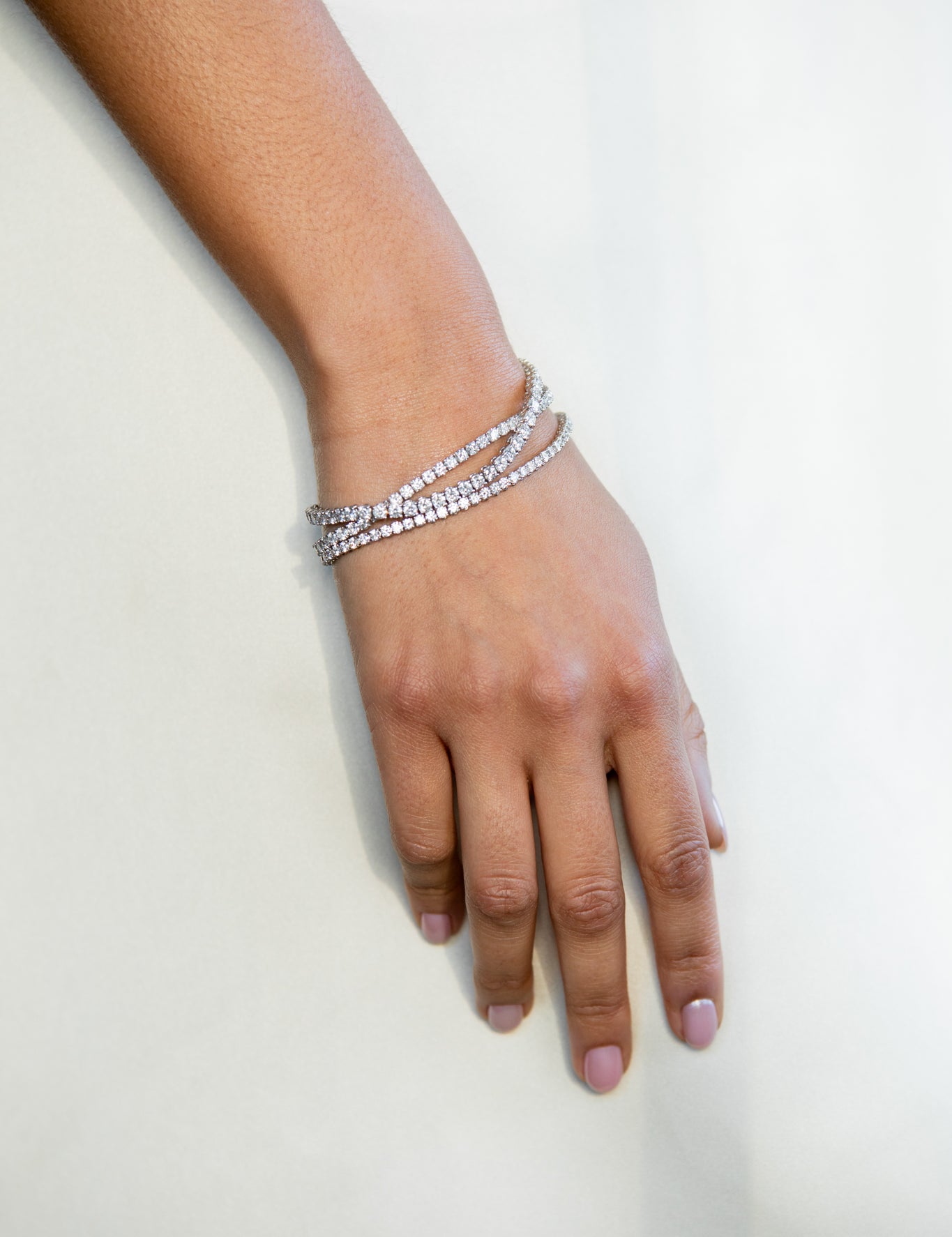 A woman's hand wearing a layered diamond bracelet against a light, neutral background.