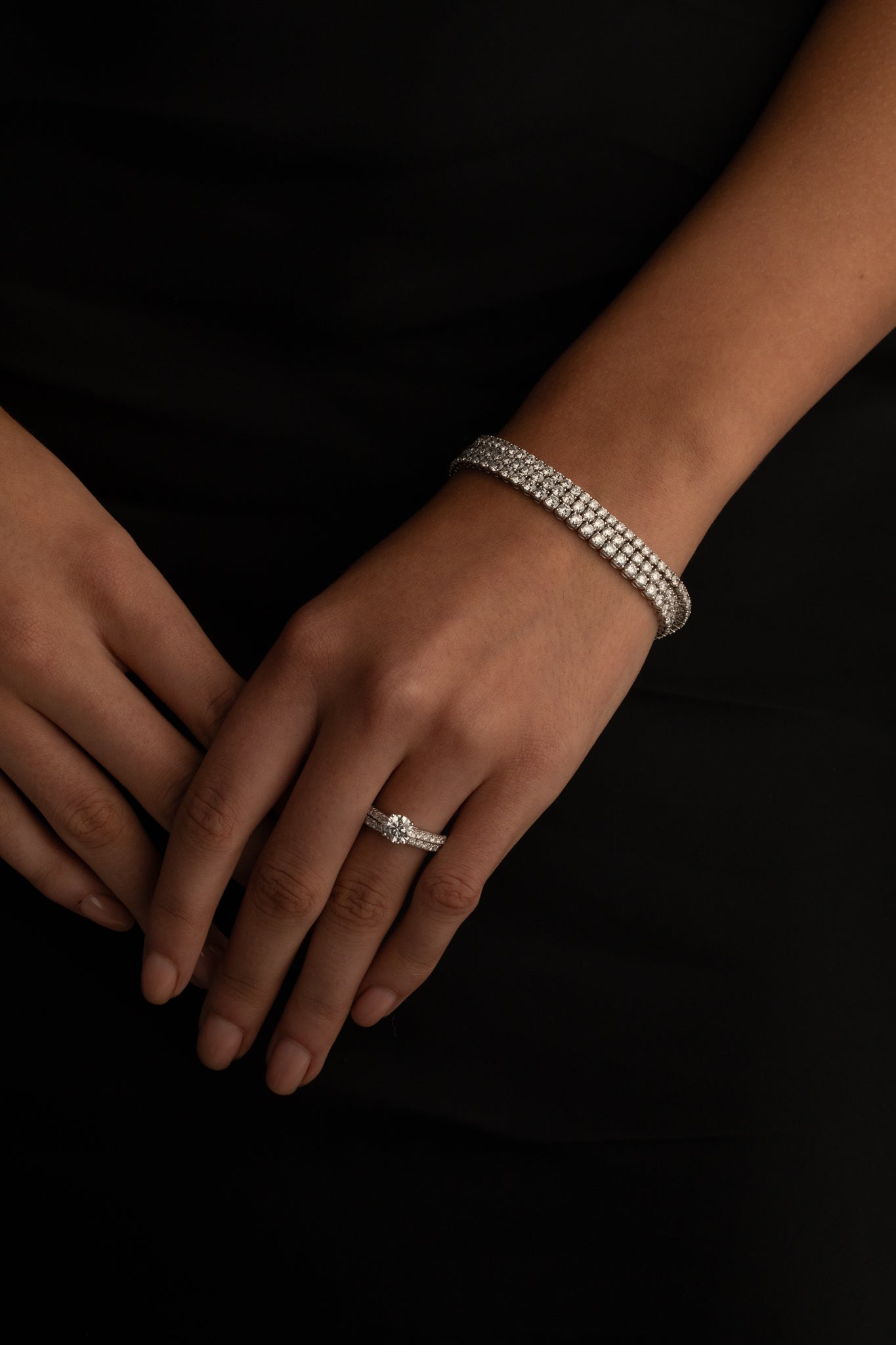 Woman's hands adorned with a diamond bracelet and matching diamond ring, styled against a black outfit.
