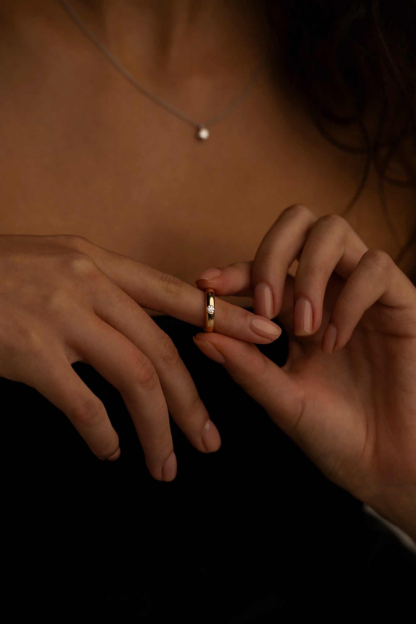 Woman wearing a delicate gold ring on her finger, with a simple pearl necklace visible, highlighting minimalist jewelry styling.