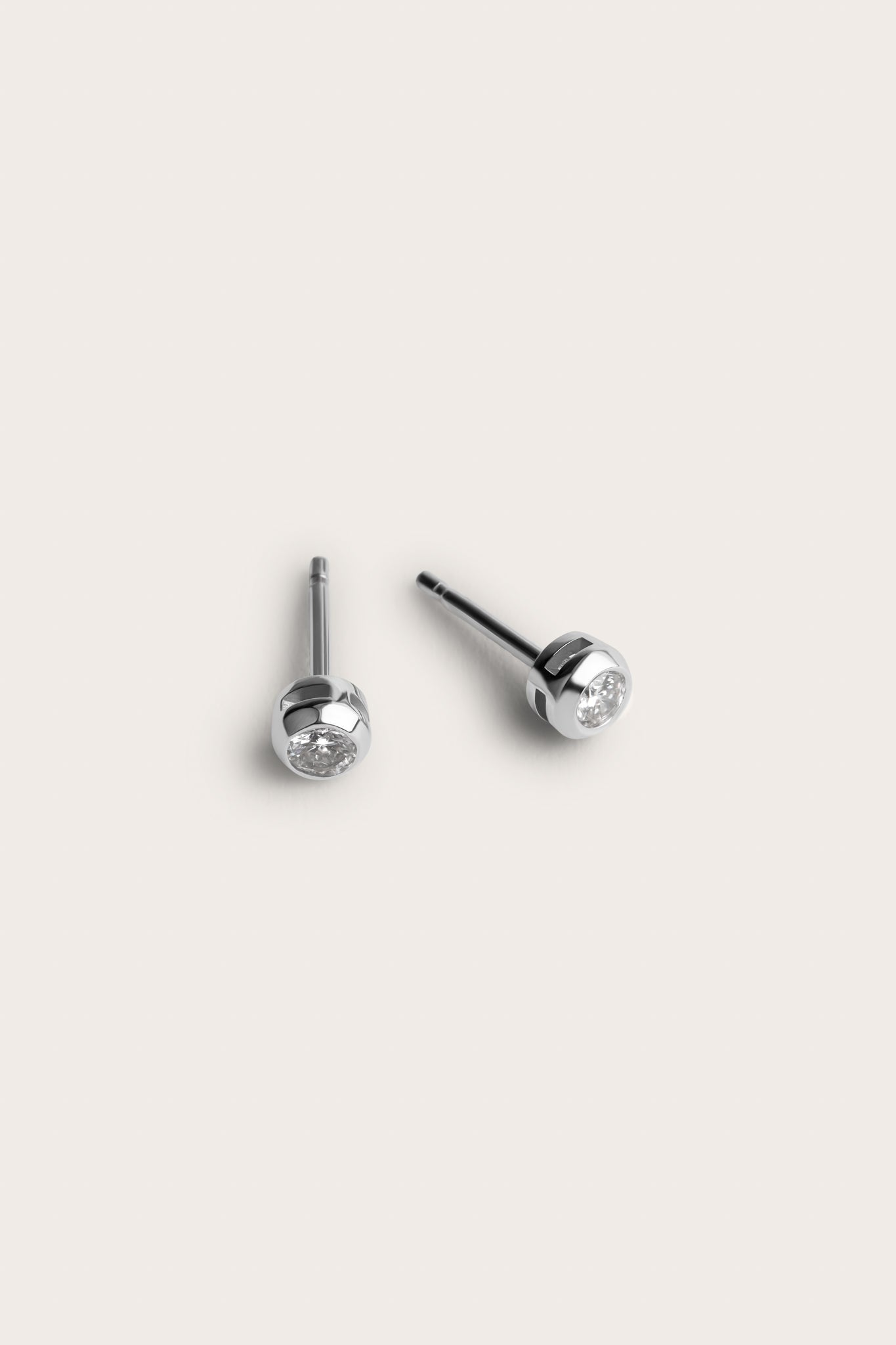 A pair of silver stud earrings featuring small, round diamonds set in a smooth, rounded bezel setting. The simple yet elegant design of the earrings showcases the diamonds at the center, giving them a subtle sparkle.