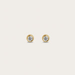 A pair of gold stud earrings featuring round diamonds set in a smooth, circular bezel setting. The earrings offer a simple and elegant look, with the diamonds placed in the center to provide a subtle shine.