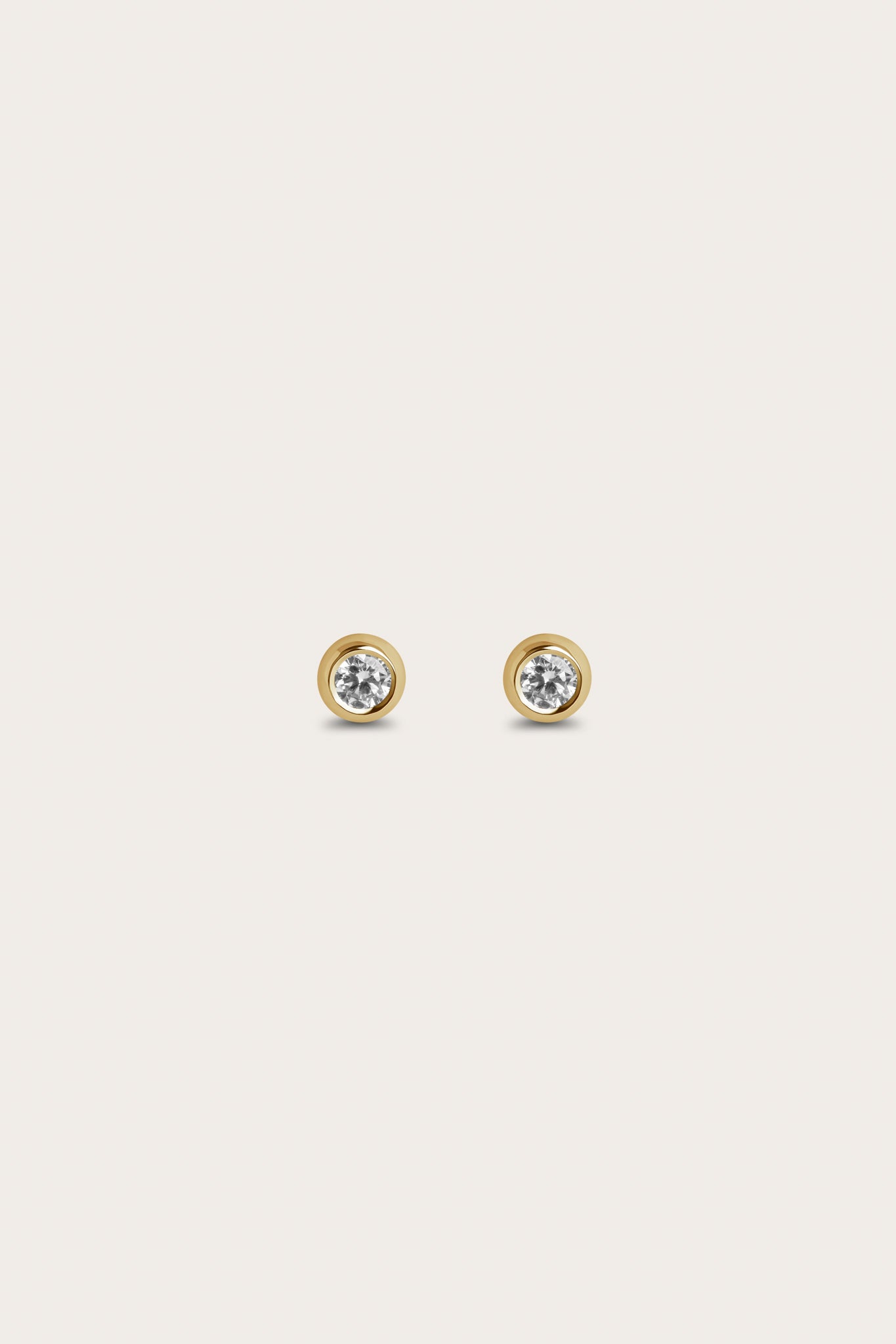 A pair of gold stud earrings featuring round diamonds set in a smooth, circular bezel setting. The earrings offer a simple and elegant look, with the diamonds placed in the center to provide a subtle shine.