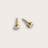 A pair of gold stud earrings featuring small, round diamond stones set in a smooth, rounded bezel setting. The earrings are simple yet elegant, with the diamonds subtly placed at the center.