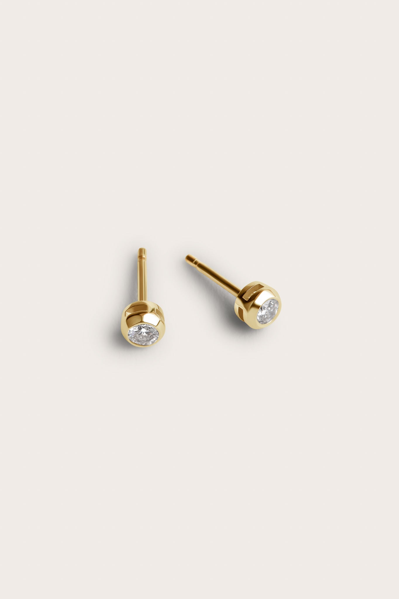 A pair of gold stud earrings featuring small, round diamond stones set in a smooth, rounded bezel setting. The earrings are simple yet elegant, with the diamonds subtly placed at the center.