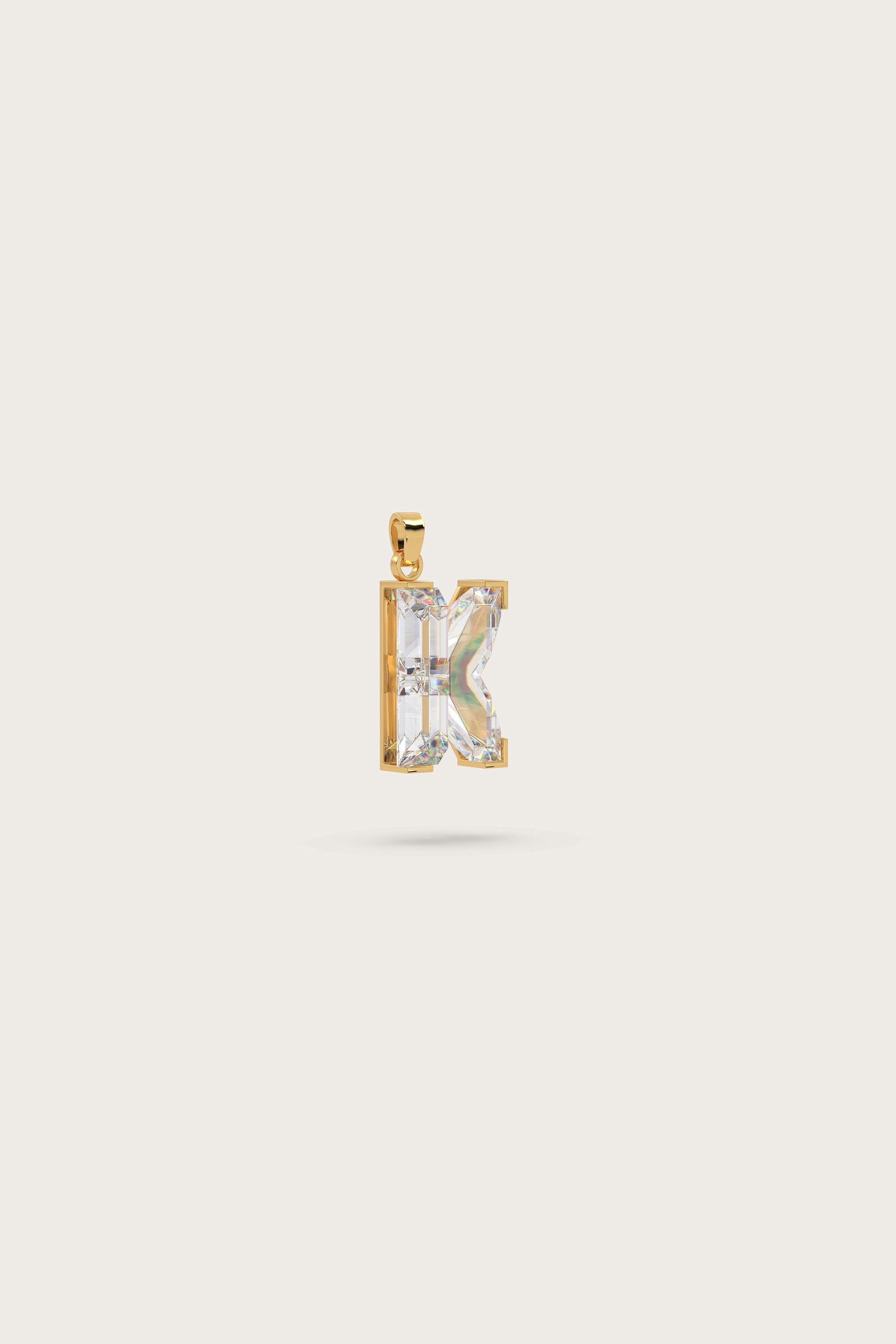 Gold pendant in the shape of the letter "K," adorned with sparkling gemstones, displayed on a light beige background.