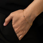 Close-up of a person wearing a delicate gold bracelet with small diamonds, resting their hand on the pocket of black clothing.