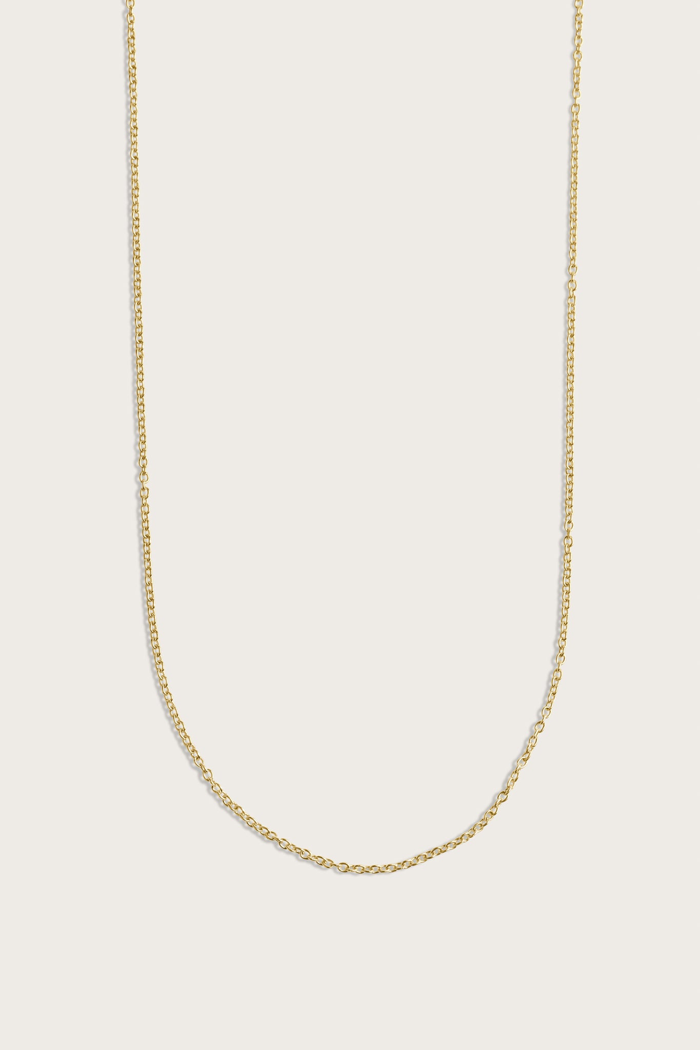 Simple gold chain necklace displayed on a light beige background.