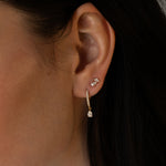 Close-up of a woman's ear wearing a small diamond stud earring and a gold drop earring with a pear-shaped diamond, paired with dark hair.