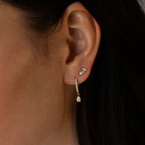 Close-up of a woman's ear wearing a small diamond stud earring and a gold drop earring with a pear-shaped diamond.