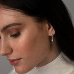 Profile view of a woman with dark hair wearing a white blouse and a silver drop earring featuring a small round diamond.