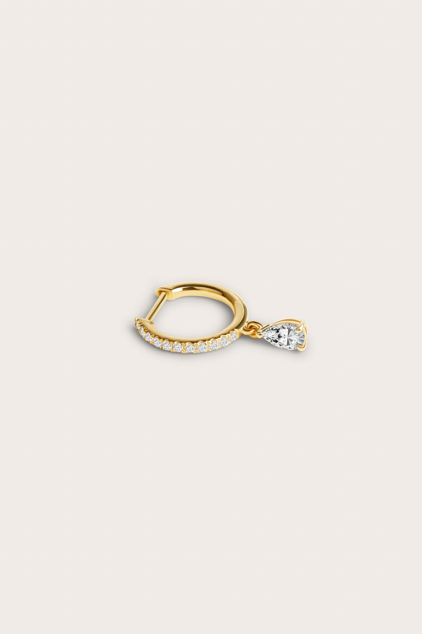 Gold hoop earring adorned with pavé-set diamonds and a dangling pear-shaped diamond, displayed on a light beige background.