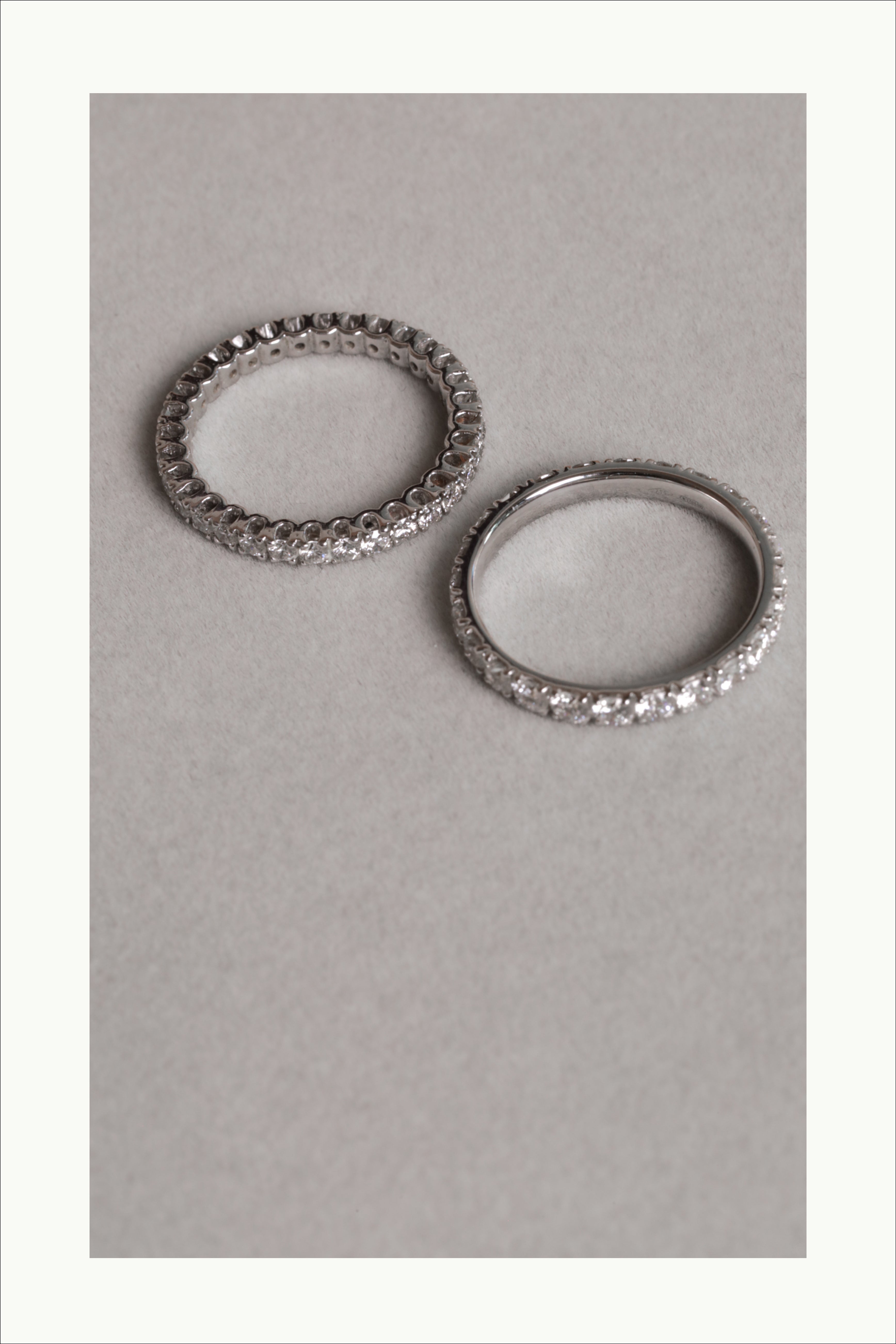 Two elegant silver eternity rings with embedded diamonds placed on a light gray surface.
