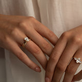 Two hands with rings featuring large center stones and diamond bands, set against a soft, neutral background, with one hand showcasing a pear-shaped diamond ring paired with a matching band, and the other hand displaying a three-stone ring.