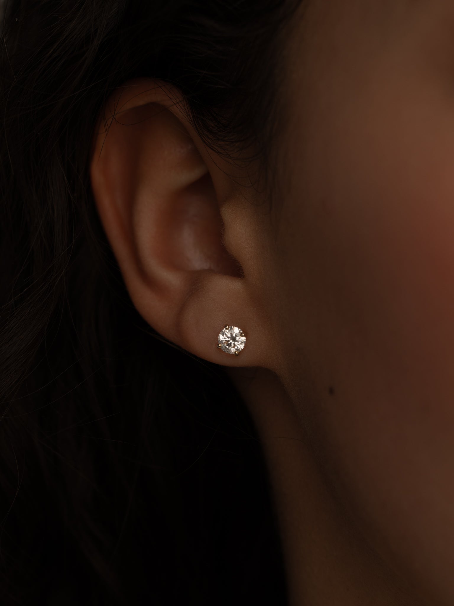 Close-up of a woman's ear wearing a single round diamond stud earring.