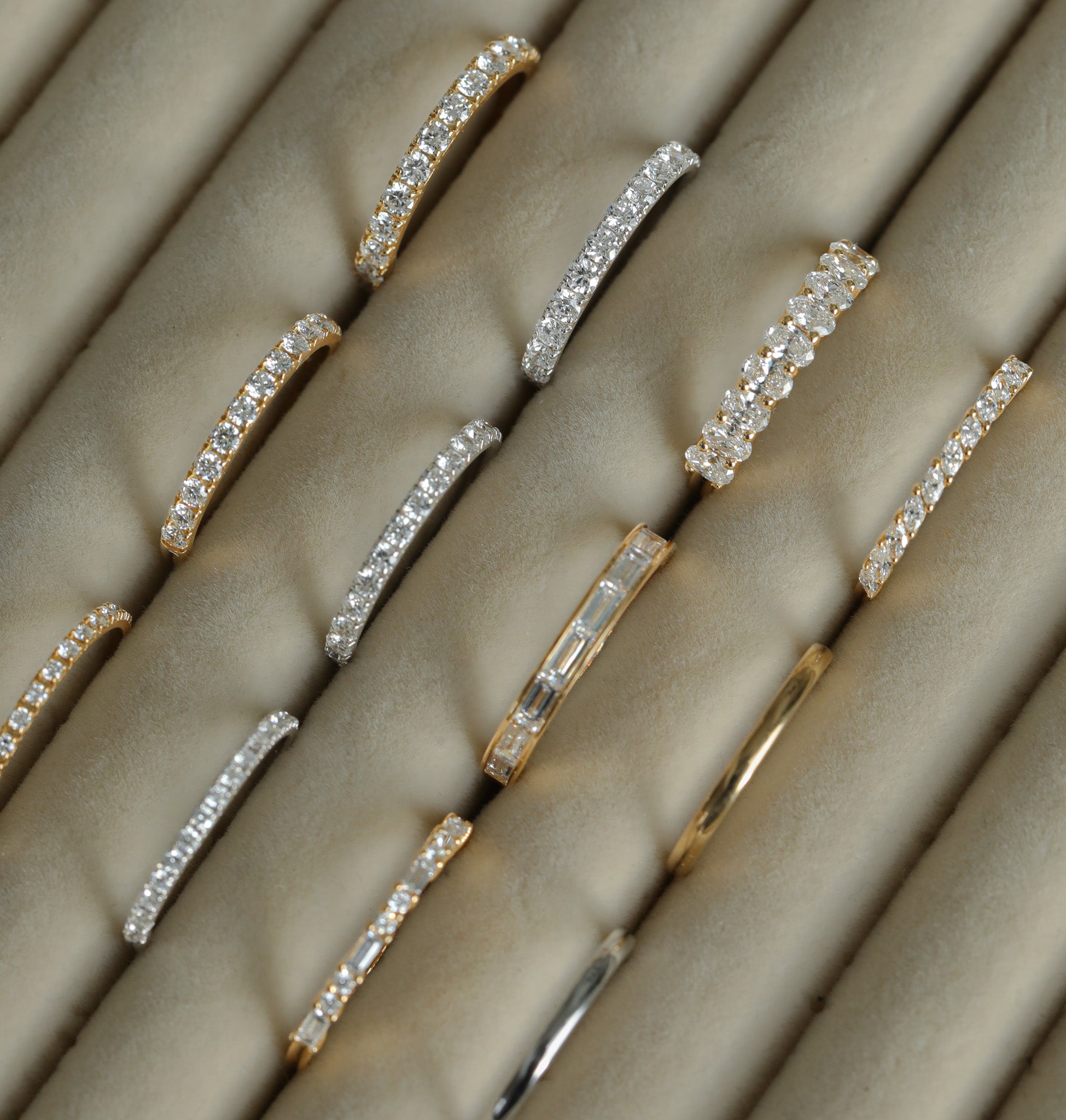 Rows of gold and silver diamond rings displayed on a soft beige jewelry tray.