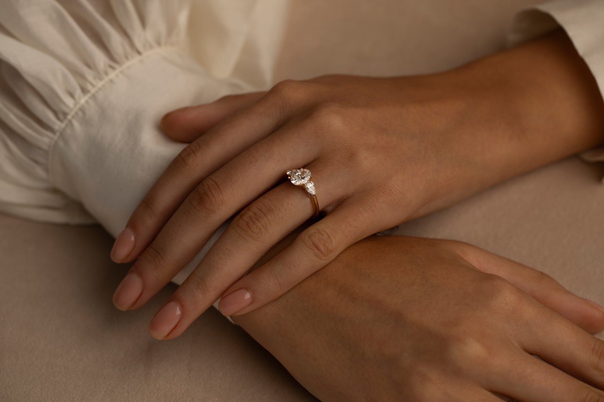 Close-up of a woman's hands resting gently, wearing an elegant diamond ring with a gold band.
