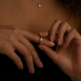 Woman wearing a delicate gold ring on her finger, with a simple pearl necklace visible, highlighting minimalist jewelry styling.