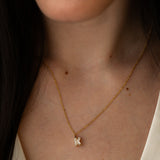 Close-up of a woman wearing a gold necklace with a diamond-studded "K" pendant, paired with a white top.