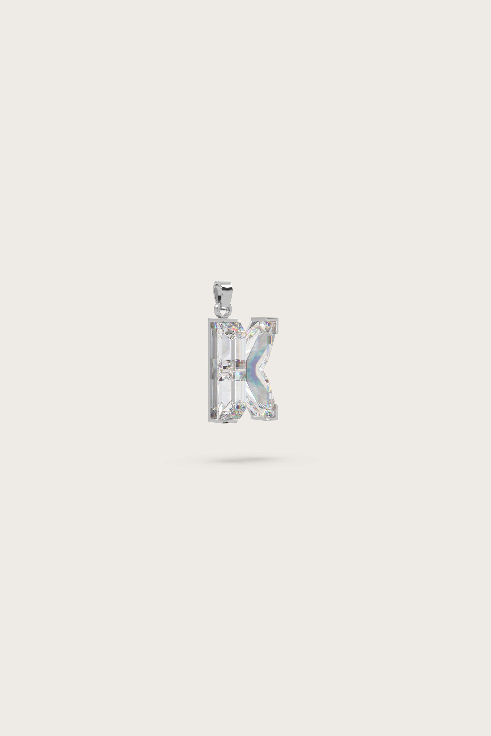 Silver pendant in the shape of the letter "K," adorned with sparkling gemstones, displayed on a light beige background.