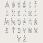 Set of silver alphabet pendants with sparkling gemstones in various cuts, arranged alphabetically on a light beige background.