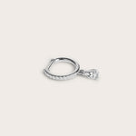 Silver hoop earring adorned with pavé-set diamonds and a dangling pear-shaped diamond, displayed on a light beige background.
