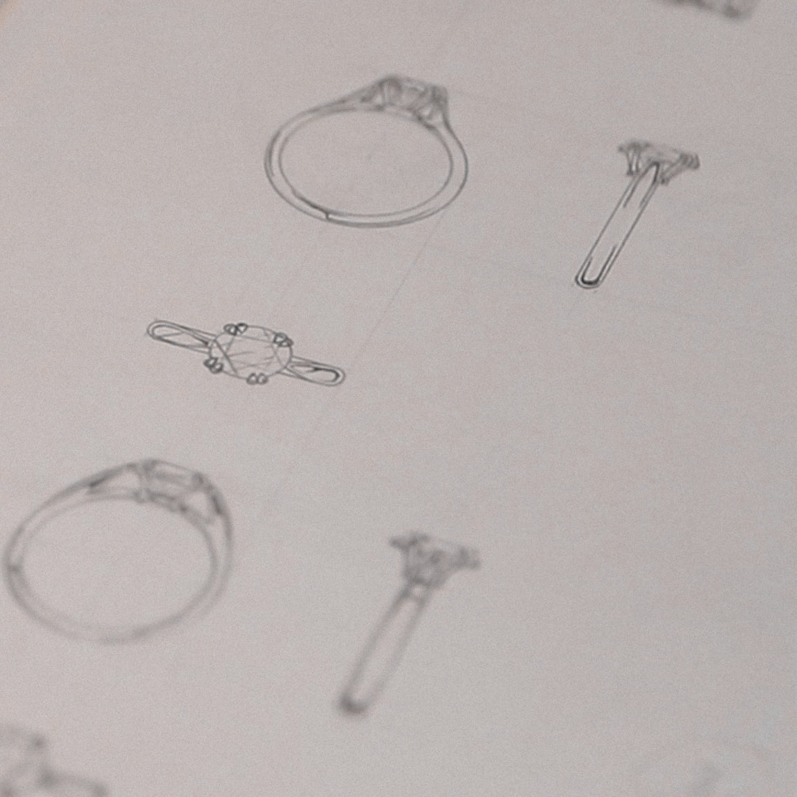 Sketches of various ring designs drawn on a sheet of paper, showcasing detailed outlines and side profiles of jewelry concepts.