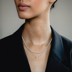 An elegant editorial lifestyle portrait of a model wearing a blazer, showcasing a luxury layering combination with a white gold bezel-set diamond necklace layered beneath a shimmering rose gold diamond tennis necklace.