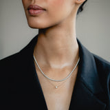 An elegant editorial lifestyle portrait of a model wearing a blazer, showcasing a luxury layering combination with a white gold bezel-set diamond necklace layered beneath a shimmering white gold diamond tennis necklace.