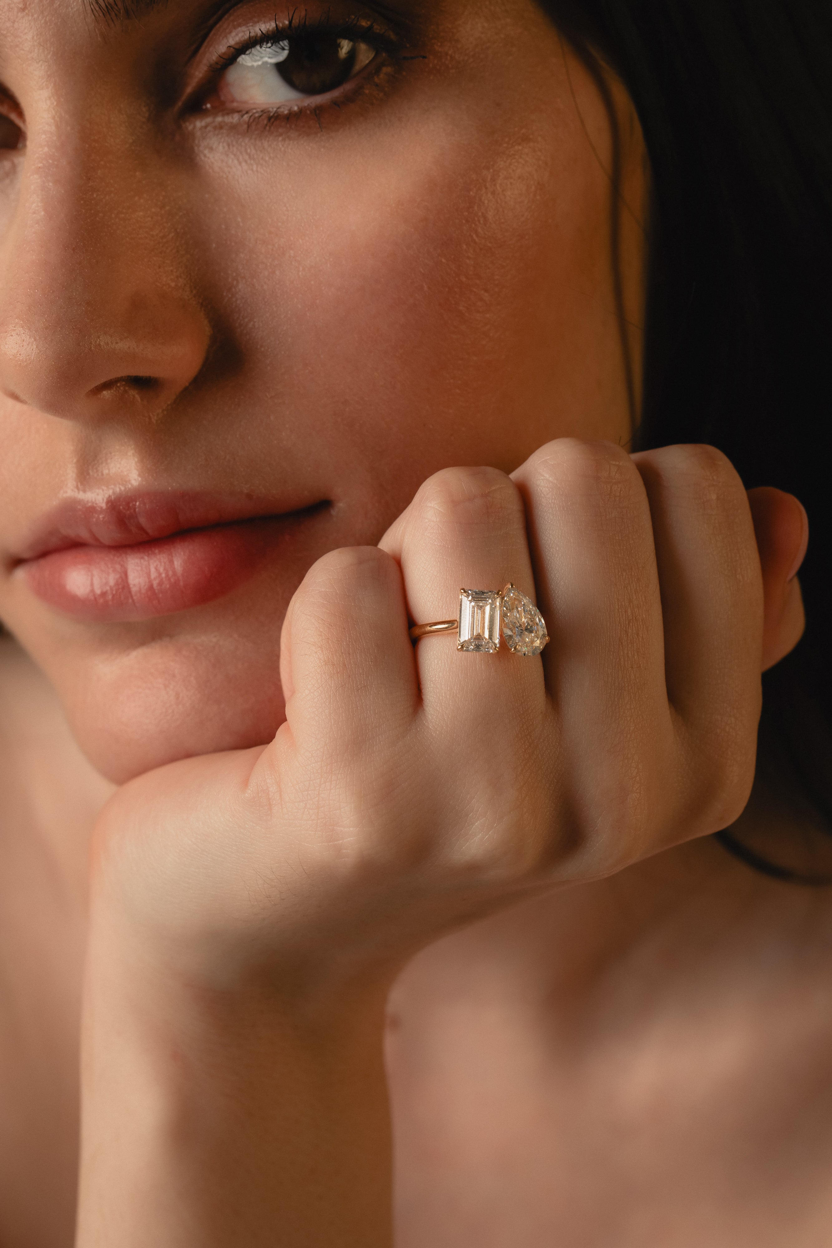 Close-up of the KARAAT Emerald and Pear Toi et Moi diamond ring in yellow gold, hand raised to the model's lips