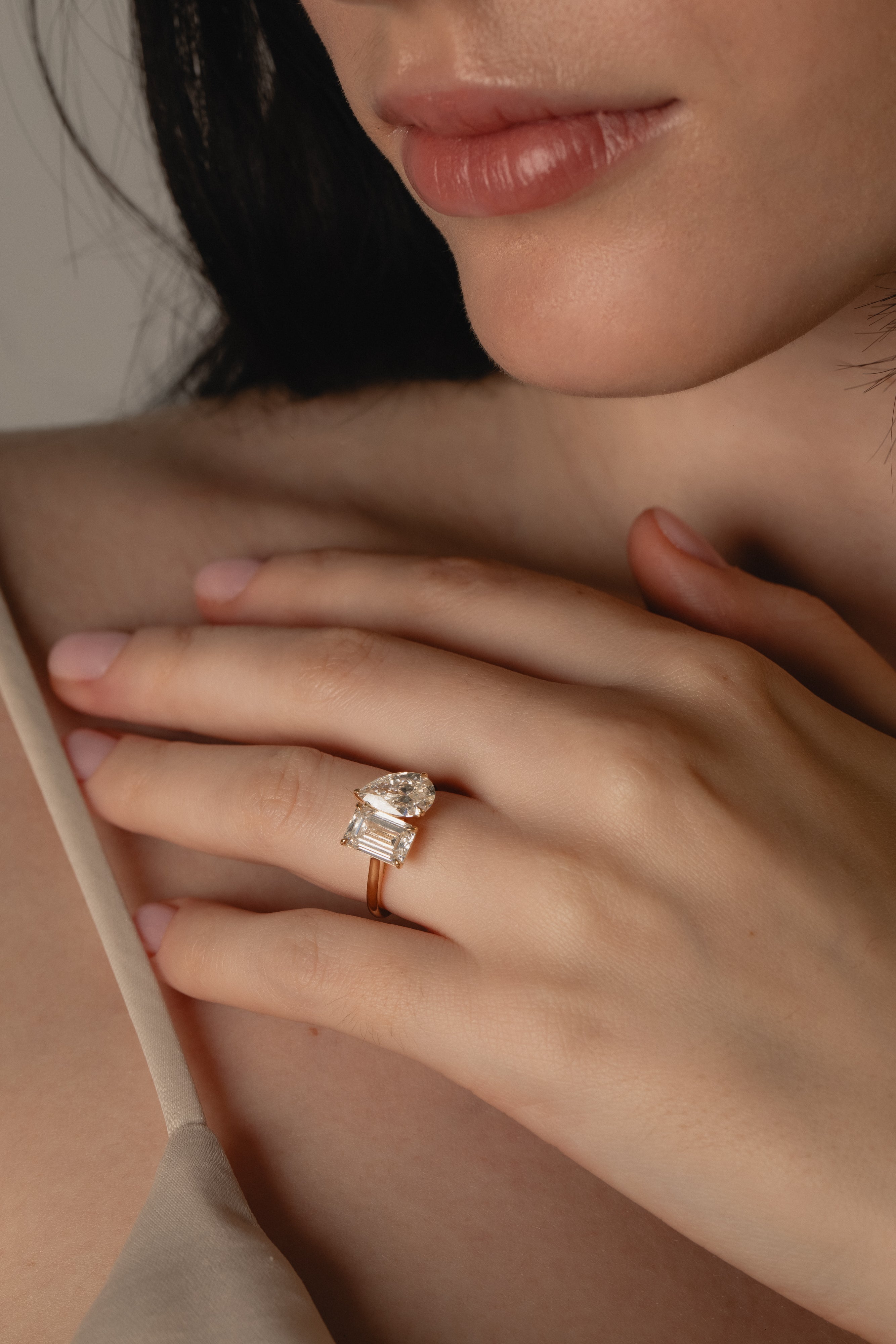 Emerald and Pear Toi et Moi lab-grown diamond engagement ring in yellow gold, hand resting at the collarbone