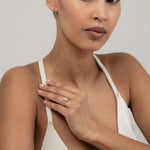 An editorial portrait of a model wearing a white strap top, elegantly displaying a yellow gold KARAAT emerald-shaped diamond solitaire ring stacked with a gold band on her finger.
