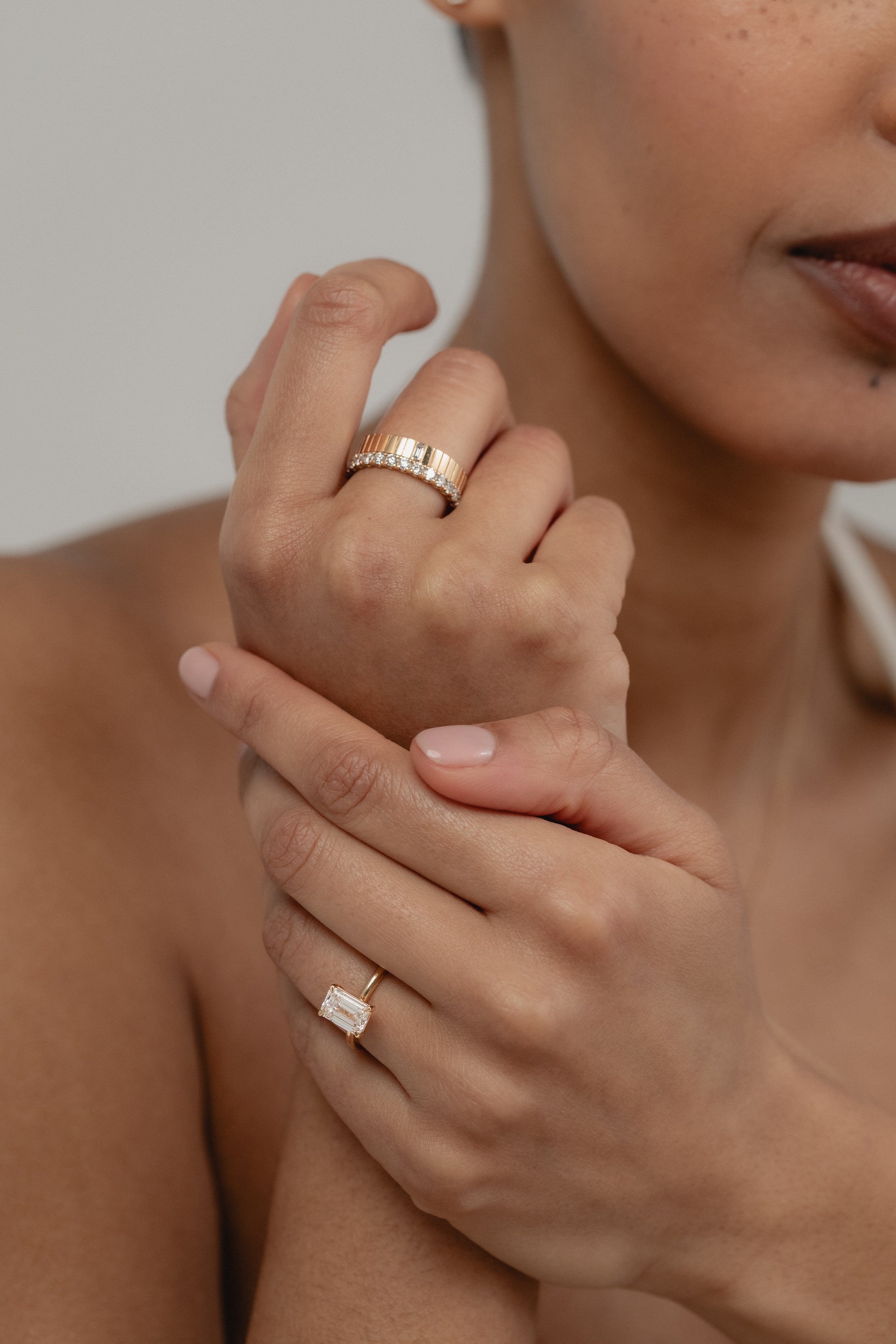 A beautiful shot of a model's crossed hands, styled with a yellow gold KARAAT emerald-cut solitaire ring on her ring finger and a bold ring stack on her index finger.