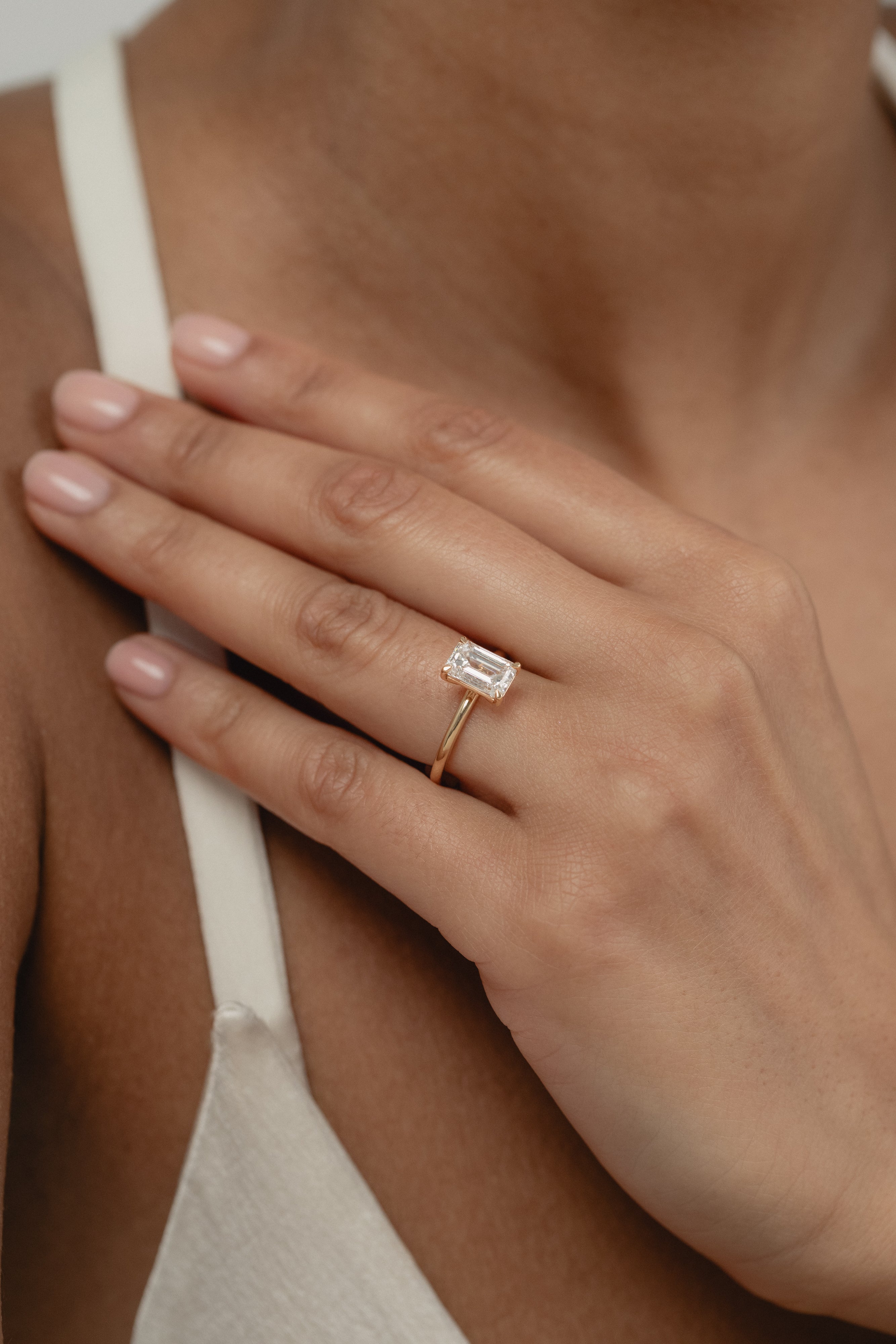 A close-up view of a model's hand showcasing the exquisite profile and setting of a KARAAT emerald-cut solitaire diamond engagement ring in 18k white gold.