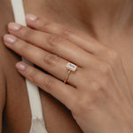 A close-up view of a model's hand showcasing the exquisite profile and setting of a KARAAT emerald-cut solitaire diamond engagement ring in 18k rose gold.