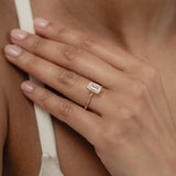 A close-up view of a model's hand showcasing the exquisite profile and setting of a KARAAT emerald-cut solitaire diamond engagement ring in 18k rose gold.