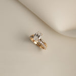 Still life shot of a white gold luxury bridal ring stack featuring a classic oval solitaire diamond engagement ring paired flush with the Pavé Diamond Ring II on a cream fabric background.