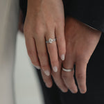 A close-up of a couple’s hands celebrating an engagement, featuring a KARAAT Oval Solitaire diamond ring with a pavé band in 18k white gold.
