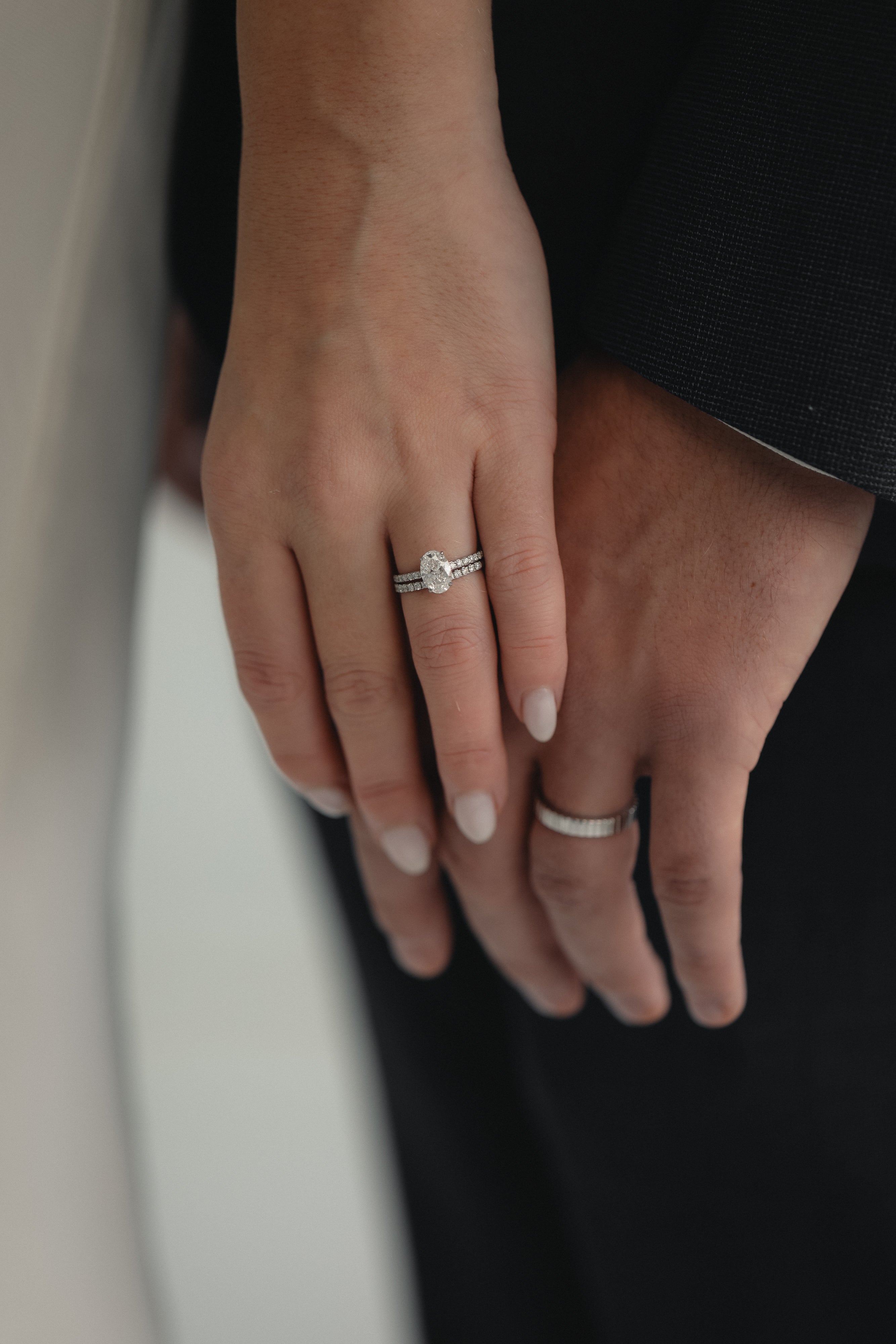 A close-up of a couple’s hands celebrating an engagement, featuring a KARAAT Oval Solitaire diamond ring with a pavé band in 18k rose gold.