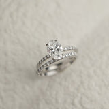 A professional still-life photograph of a KARAAT's oval-cut diamond solitaire engagement ring with a sparkling pavé band in 18k white gold, displayed on a neutral background.