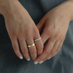 Detail shot of a model's hands gently clasped over a slate blue dress, showing a modern mixed stack featuring a wide solid gold band paired with the striking Pavé Diamond Ring III in white gold.