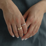 Detail shot of a model's hands gently clasped over a slate blue dress, showing a modern mixed stack featuring a wide solid gold band paired with the striking Pavé Diamond Ring III in white gold.