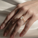 A soft-focus bridal image of a model's hand on shimmering white silk, showcasing a classic white gold oval solitaire diamond engagement ring nested flush beside a delicate KARAAT pavé diamond wedding band.