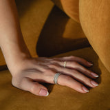 Sunlit detail shot of a model's hand resting on golden ochre fabric, showcasing a prominent ring stack featuring a thick diamond eternity band layered with a delicate classic rose gold pavé diamond ring.