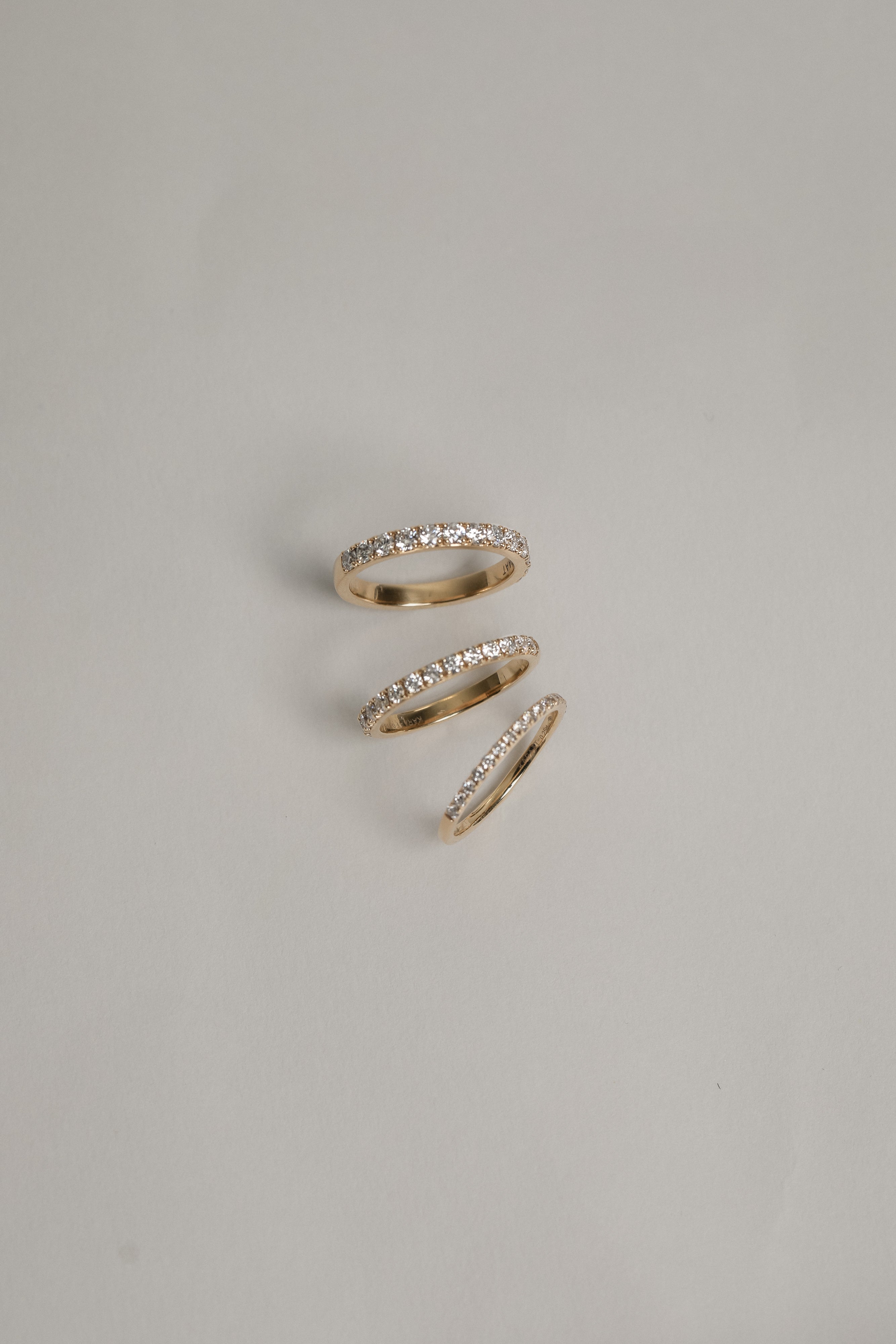A clean flat-lay product shot displaying three KARAAT pavé diamond rings on a light grey background, showcasing different band widths and diamond carat sizes in polished rose gold.