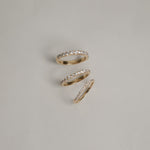 A clean flat-lay product shot displaying three KARAAT pavé diamond rings on a light grey background, showcasing different band widths and diamond carat sizes in polished white gold.