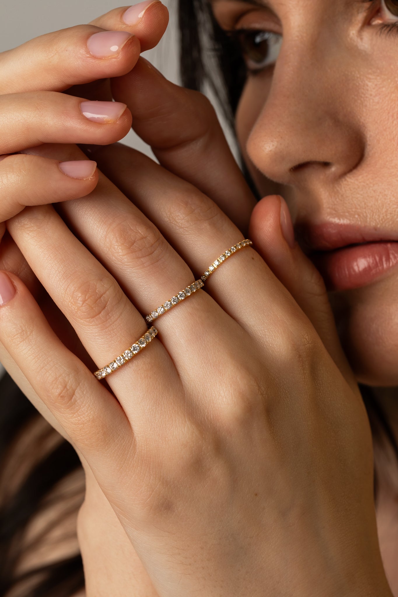 A close-up lifestyle image of a model displaying a delicate ring stack featuring multiple sizes of KARAAT yellow gold pavé diamond rings.