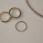 Yellow gold diamonds rings on a light gray surface with a tennis bracelet next to them.