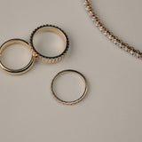 Rose gold diamonds rings on a light gray surface with a tennis bracelet next to them.