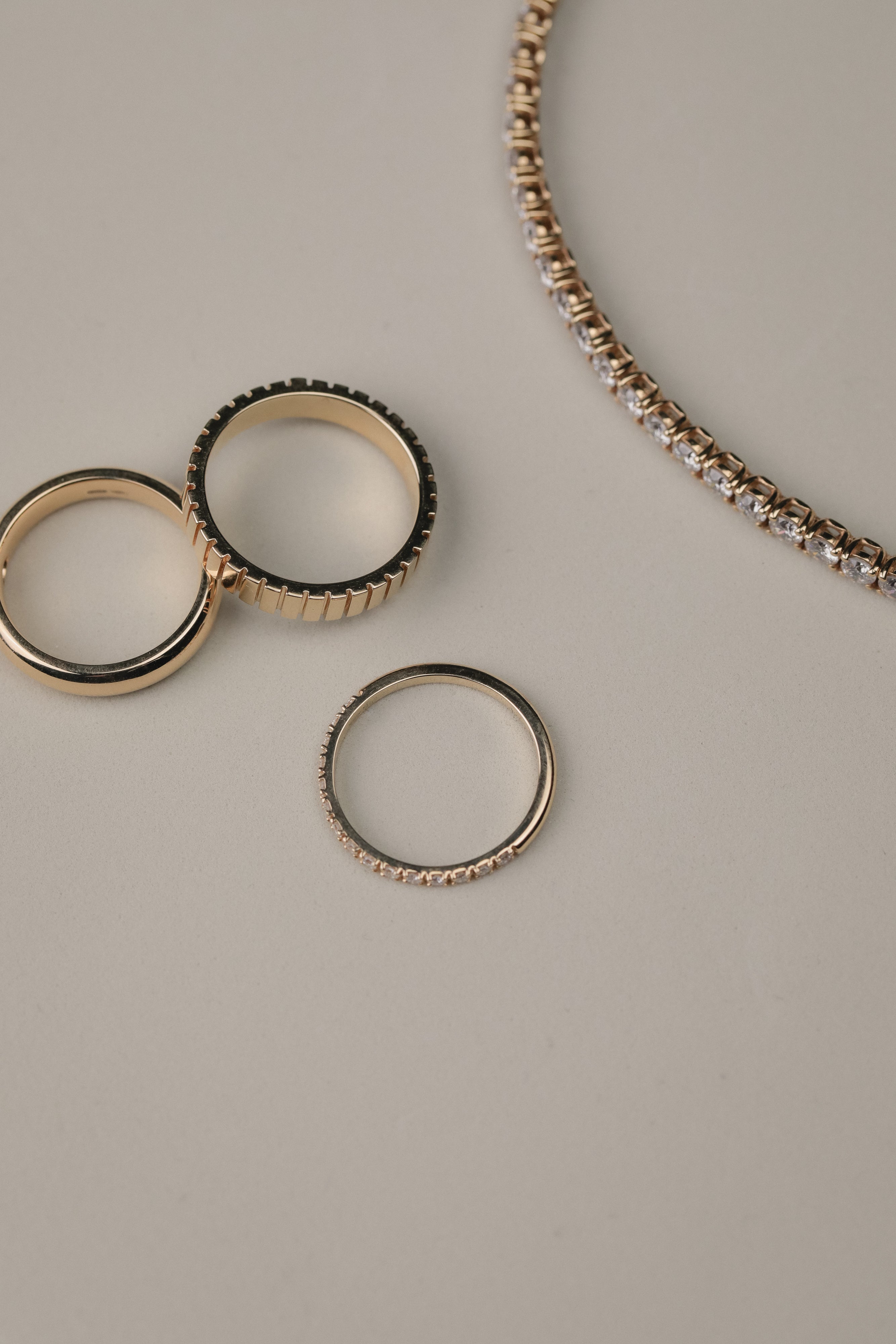White gold diamonds rings on a light gray surface with a tennis bracelet next to them.