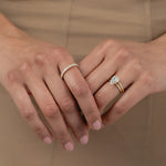 A close-up of a model's hands crossed against a beige dress, styled with a rose gold KARAAT pear-shaped diamond solitaire ring stacked with a gold band on one hand, and a radiant-cut diamond half eternity band on the other.